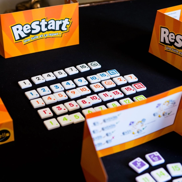 🔸Restart🔸
(Fr & En)

@iello_fr 

👀 Comment on joue ?

Restart est un jeu de pose de tuiles tactique et accessible dans lequel les joueurs doivent se débarrasser de leurs tuiles numérotées le plus rapidement possible. Pour y parvenir, ils vont construire des suites croissantes par couleur au centre de la table… tout en essayant de bloquer leurs adversaires au bon moment.

1. Mise en place
Chaque joueur reçoit un ensemble de tuiles numérotées qu’il place cachées derrière son paravent.
Au centre de la table, plusieurs lignes de couleurs sont créées, chacune commençant par le chiffre 1.

2. Déroulement d’un tour
À son tour, un joueur a plusieurs options :

➡Poser des tuiles
Le joueur peut poser une ou plusieurs tuiles consécutives de même couleur sur une ligne correspondante.

- Les valeurs doivent toujours être croissantes
- Il est possible de jouer plusieurs tuiles d’un coup pour accélérer son jeu

C’est le cœur du jeu : optimiser ses poses pour se débarrasser rapidement de ses tuiles.

➡Jouer une tuile spéciale
Certaines tuiles permettent de complètement changer la situation :

- supprimer la dernière tuile d’une ligne
- vider une ligne presque entièrement
- bloquer définitivement une ligne
- ou au contraire la redémarrer à zéro

Ces effets apportent une forte interaction et créent des retournements de situation permanents

➡Passer son tour
Si aucun coup intéressant n’est possible, le joueur peut passer… mais cela peut lui coûter cher s’il garde trop de tuiles.

3. Fin d’une manche
Une manche se termine lorsque :

un joueur n’a plus de tuiles

ou que tous les joueurs passent

Les joueurs additionnent alors la valeur des tuiles restantes en main, ce qui constitue des points négatifs.

4. Fin de partie
La partie se termine lorsqu’un joueur atteint le seuil de points défini (souvent 100).
Le joueur avec le score le plus faible remporte la partie.
.
.
.
Copie presse
